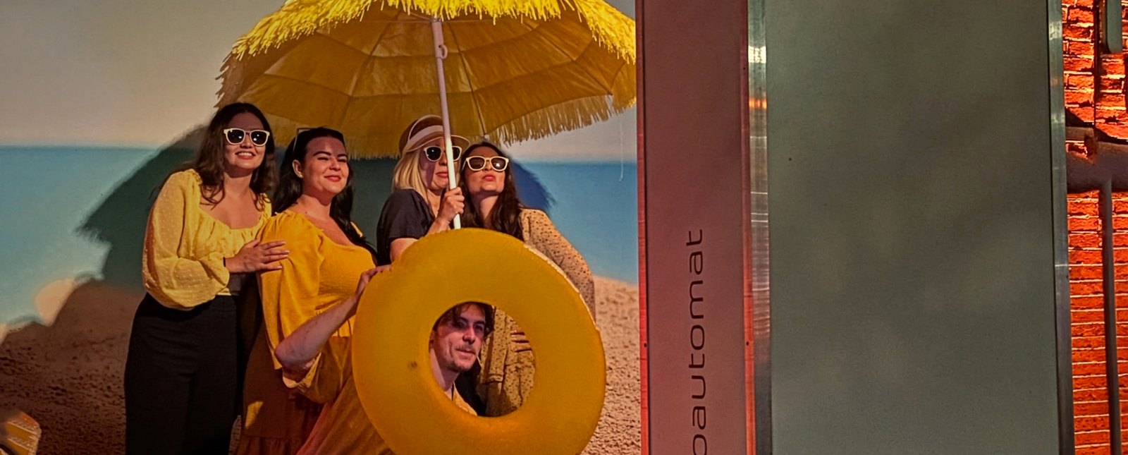 Gäste mit Sonnenschirm und Schwimmreifen vor dem Fotoautomaten von Flash-U