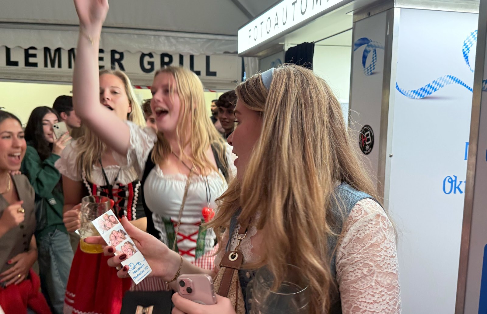 Gruppe in Dirndl lacht vor dem Fotoautomaten von Flash-U und hält den frisch gedruckten Fotostreifen vom Münsteraner Oktoberfest hoch