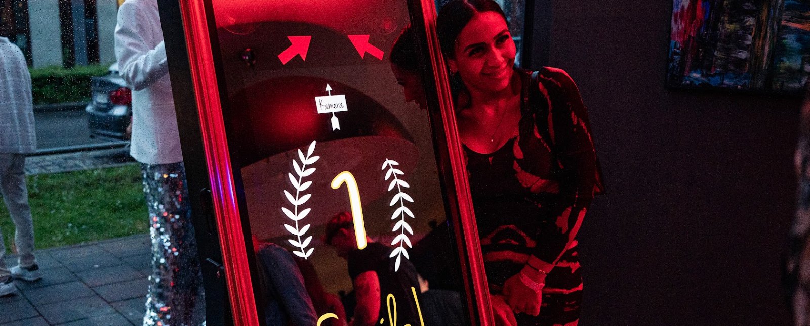 Lächelnde Frau neben der Spiegel-Fotobox von Flash-U, der Bildschirm zeigt den Countdown mit Smile