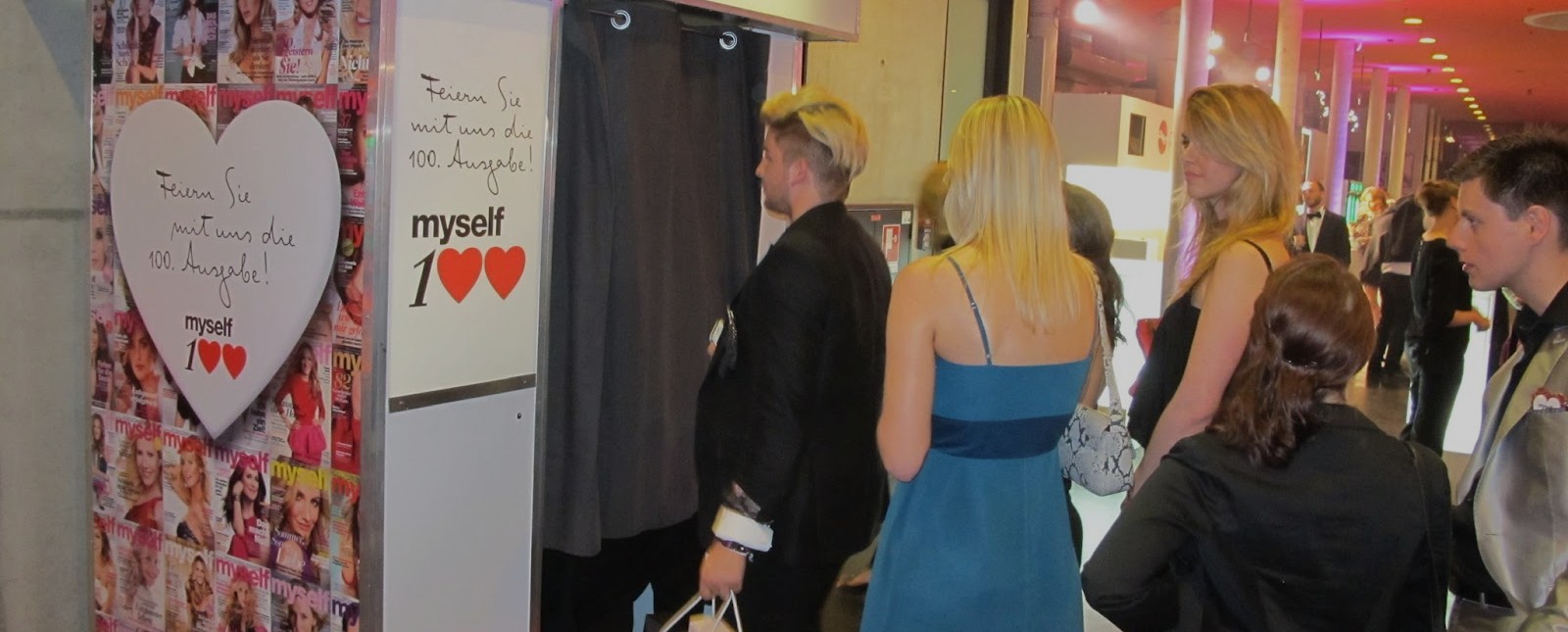 Gäste in Abendgarderobe warten abends an der Fotobox — festlich beleuchtetes Foyer