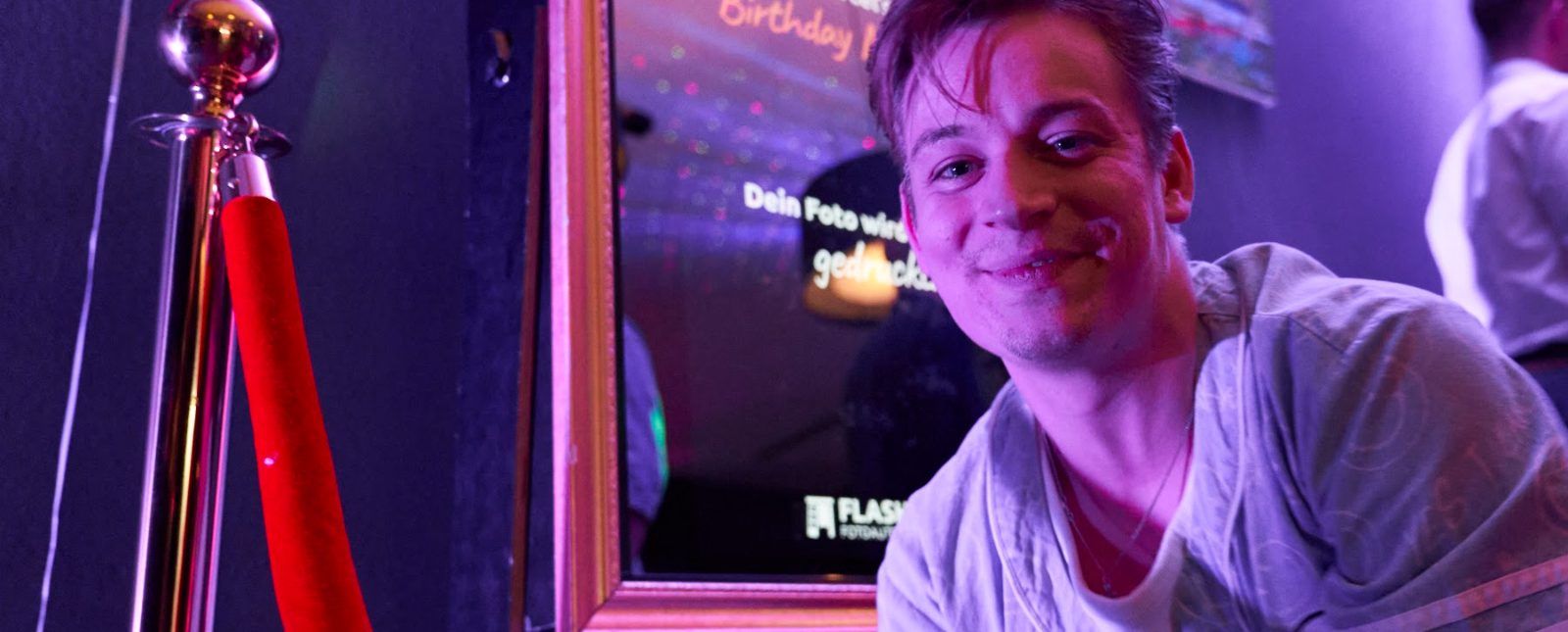 Lachender junger Mann neben dem Spiegel-Fotoautomaten von Flash-U auf einer Feier
